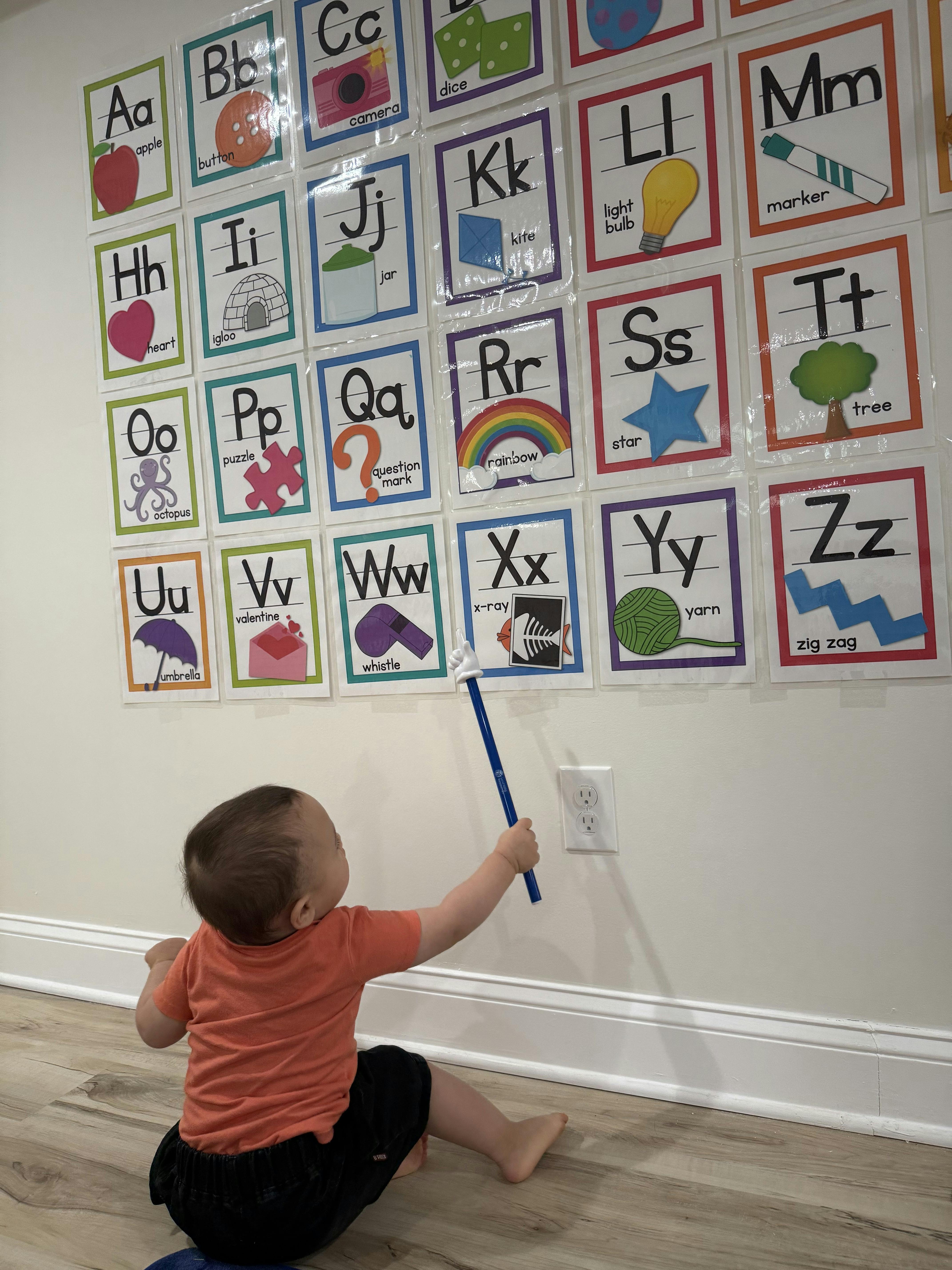 Child pointing a stick at an alphabet chart on a wall