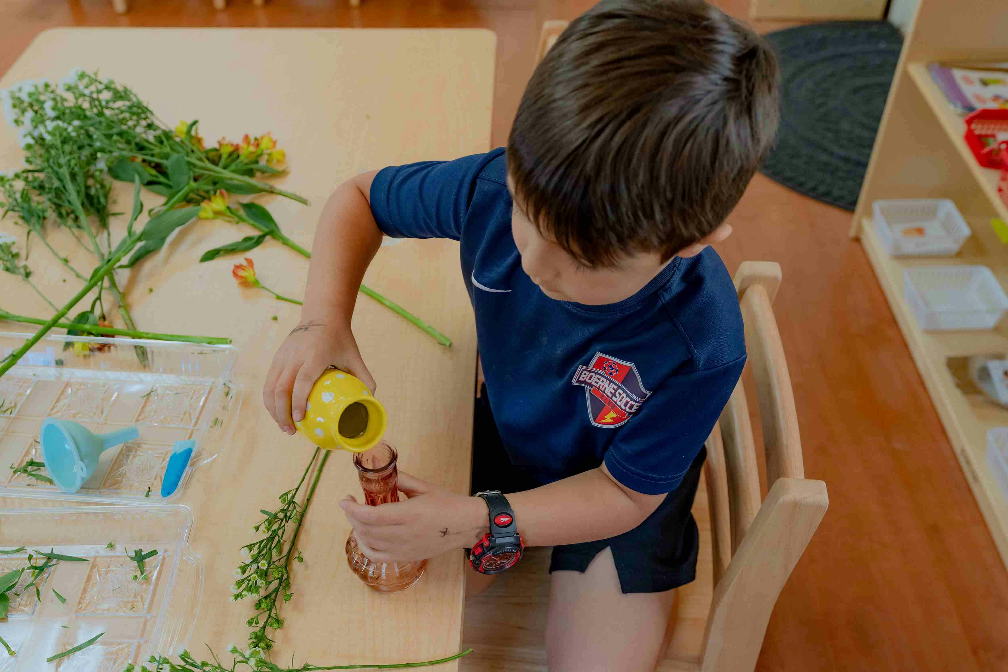 Child pouring from a small yellow container into a brown bottle at a table