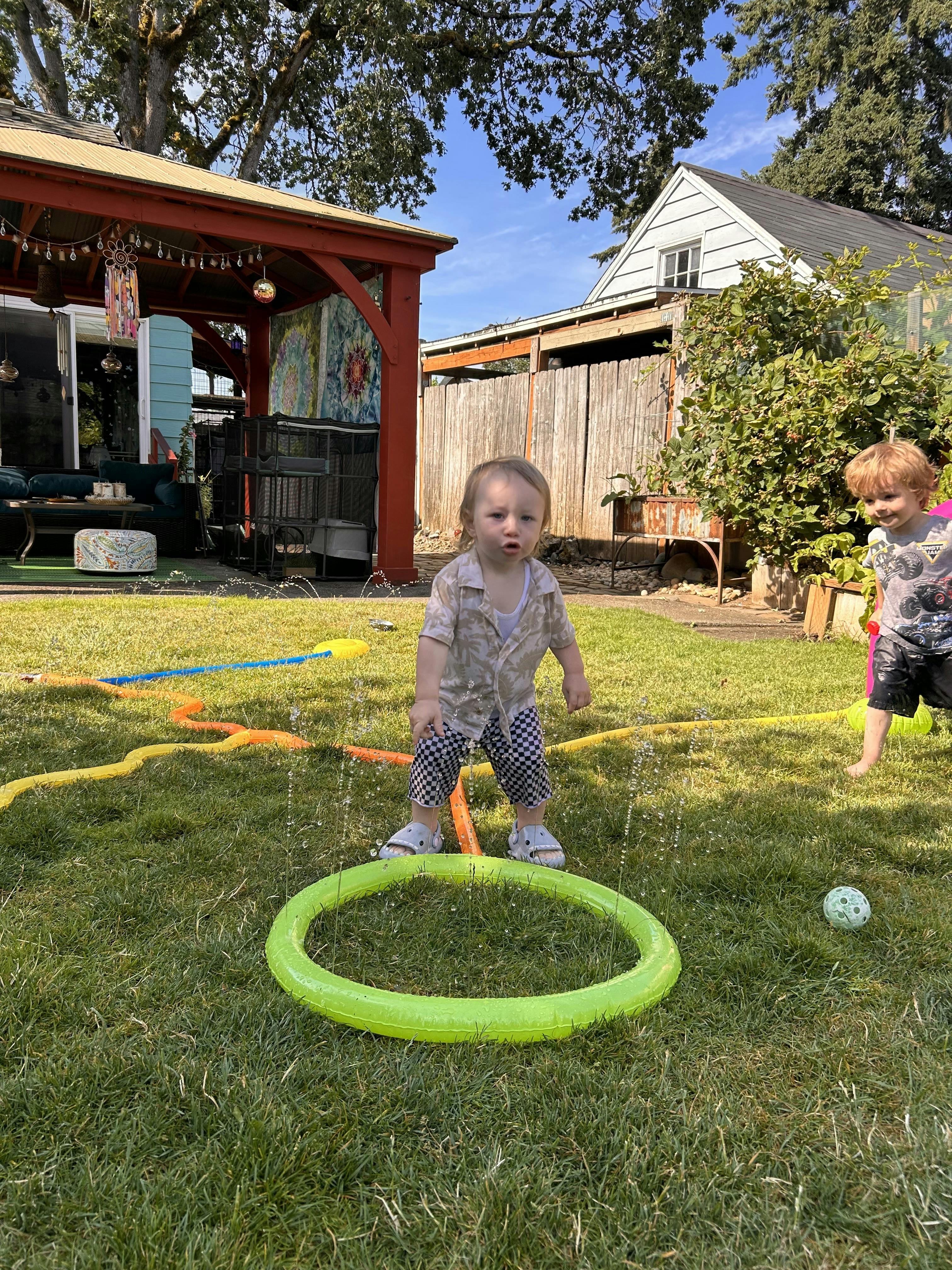 Two children playing with a water sprinkler in a backyard