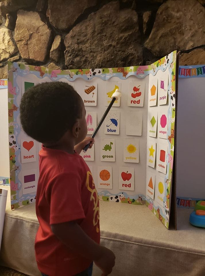 Child pointing a wand at a display board with cards showing colors and shapes
