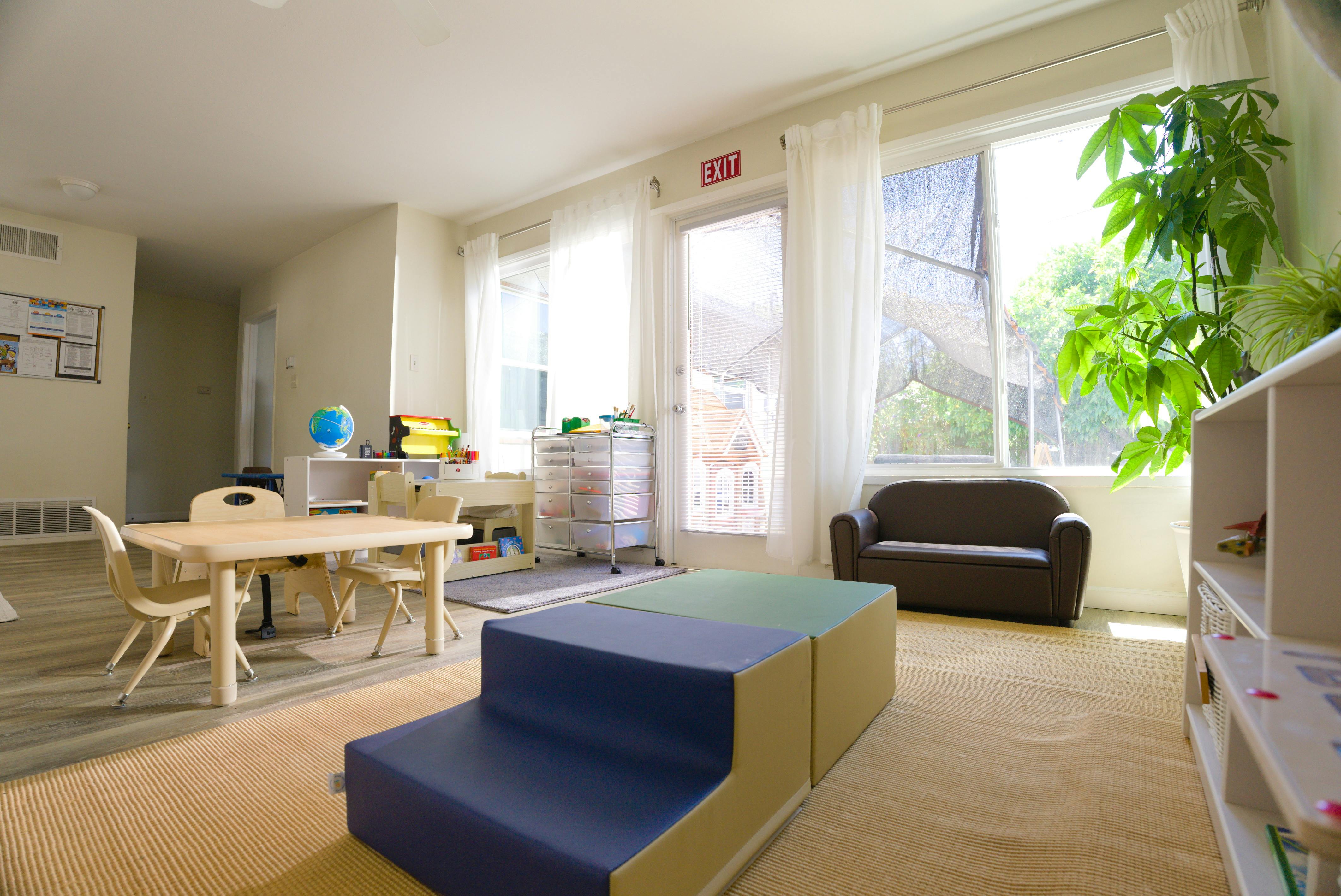 A room with small tables and chairs, a play structure, and an "EXIT" sign