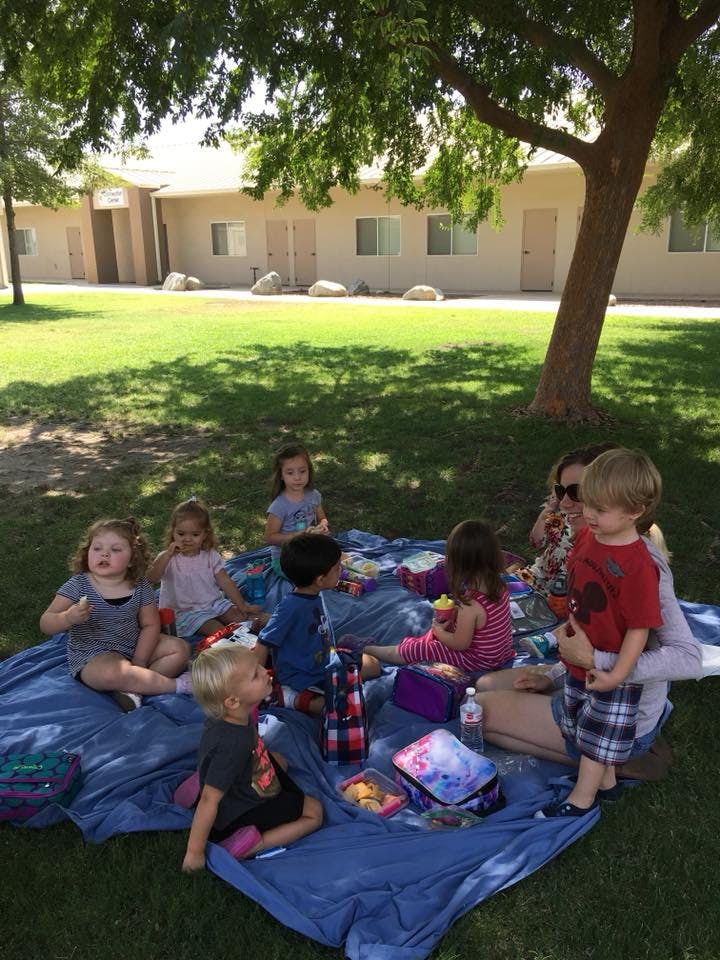 Children and adults sitting on a blue blanket on grass