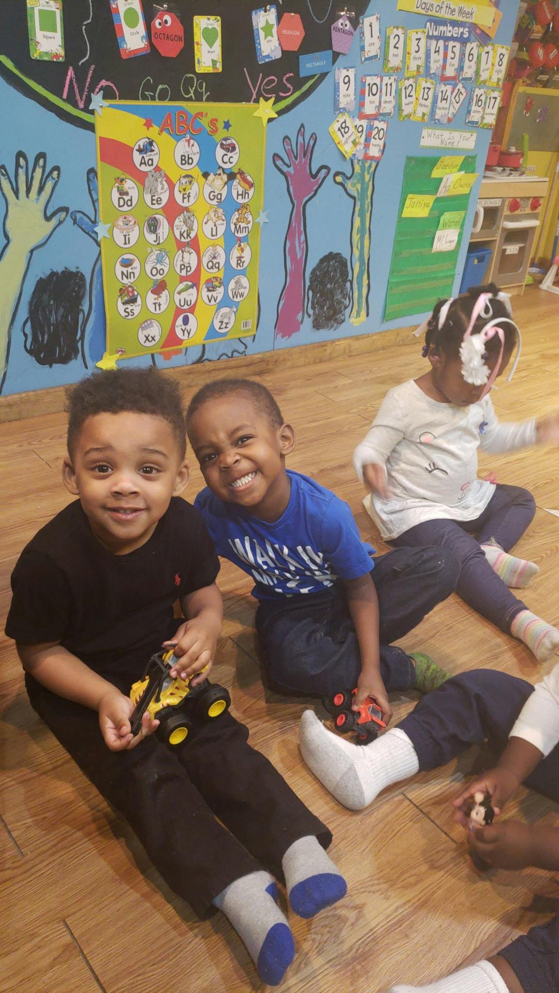 Three children sitting on a wooden floor in a classroom