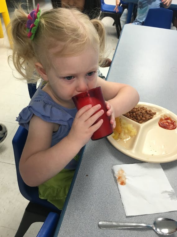 Child drinking from a red cup at a table with a divided plate of food