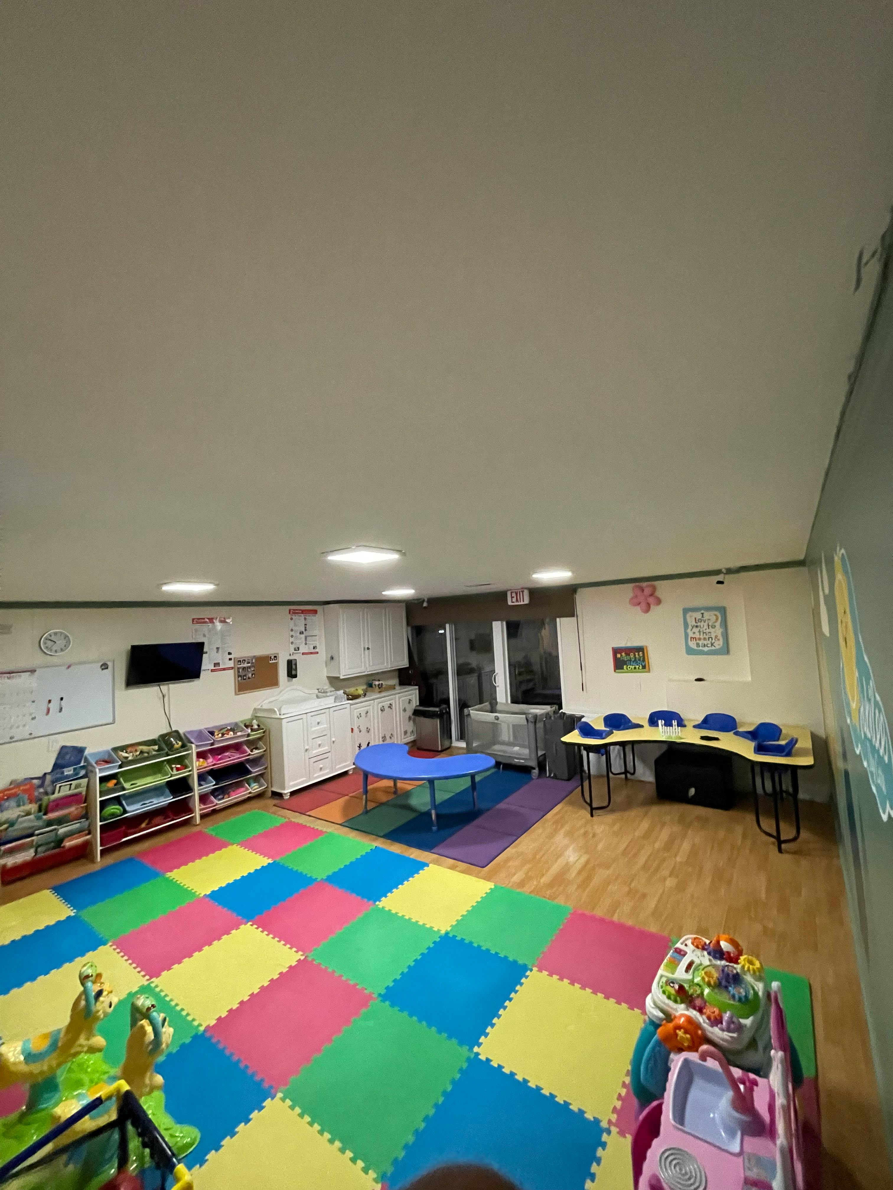 Playroom with colorful floor mats, small tables, and shelves with toys