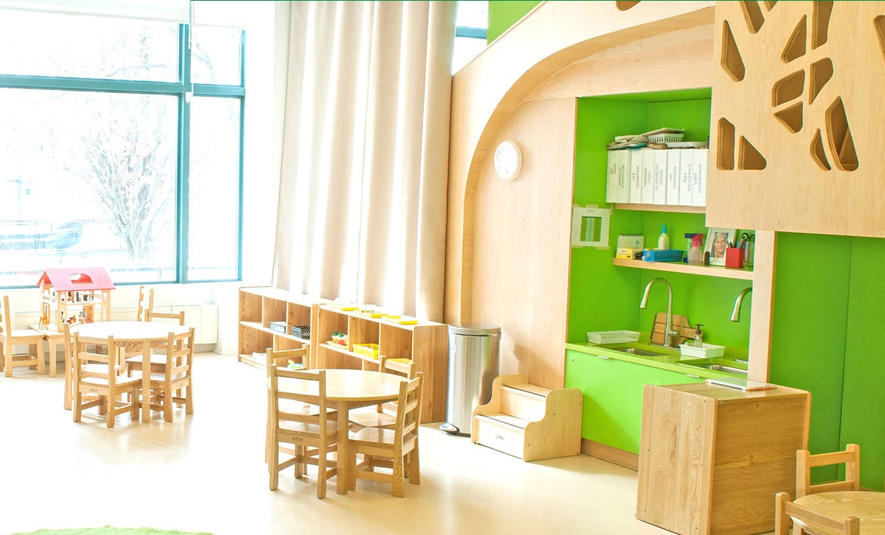 Empty classroom with small wooden tables and chairs, green shelves