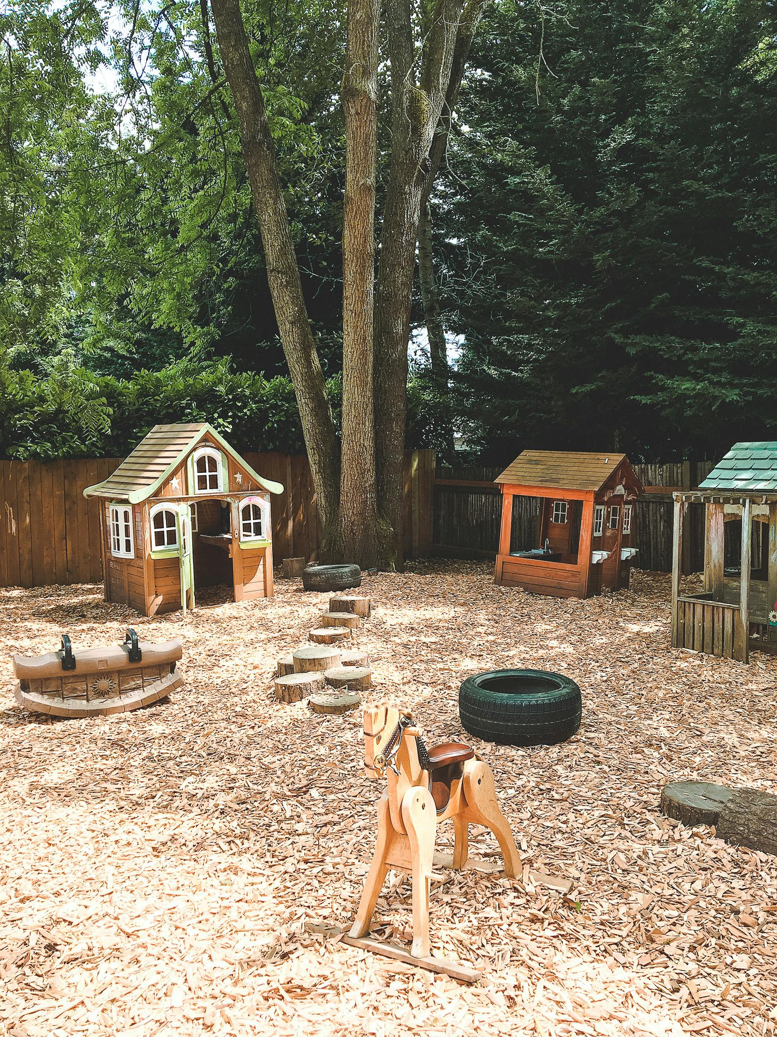 Outdoor playground with playhouses, wooden steps, and a rocking horse