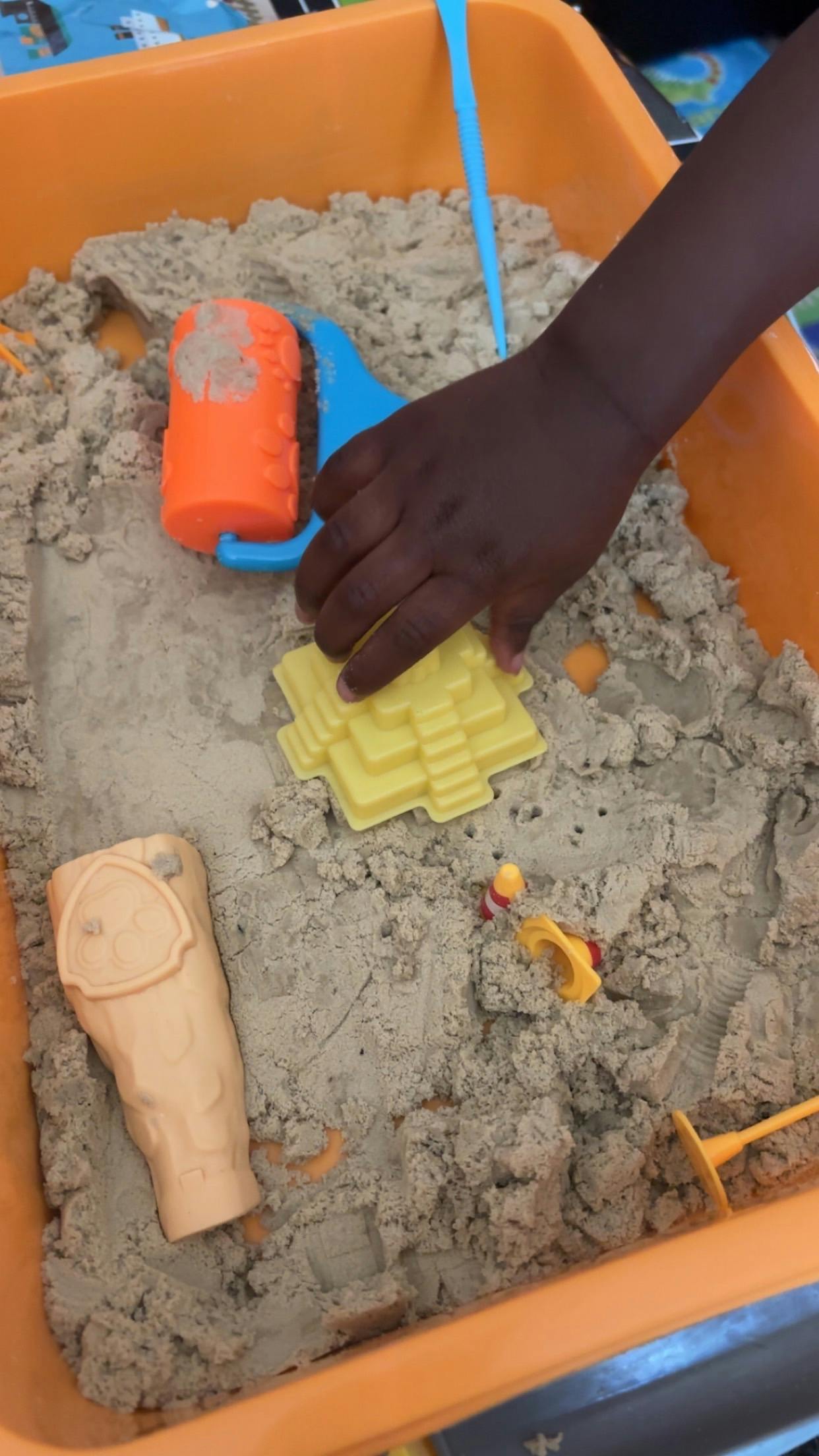 Child playing with plastic molds in a bin of kinetic sand