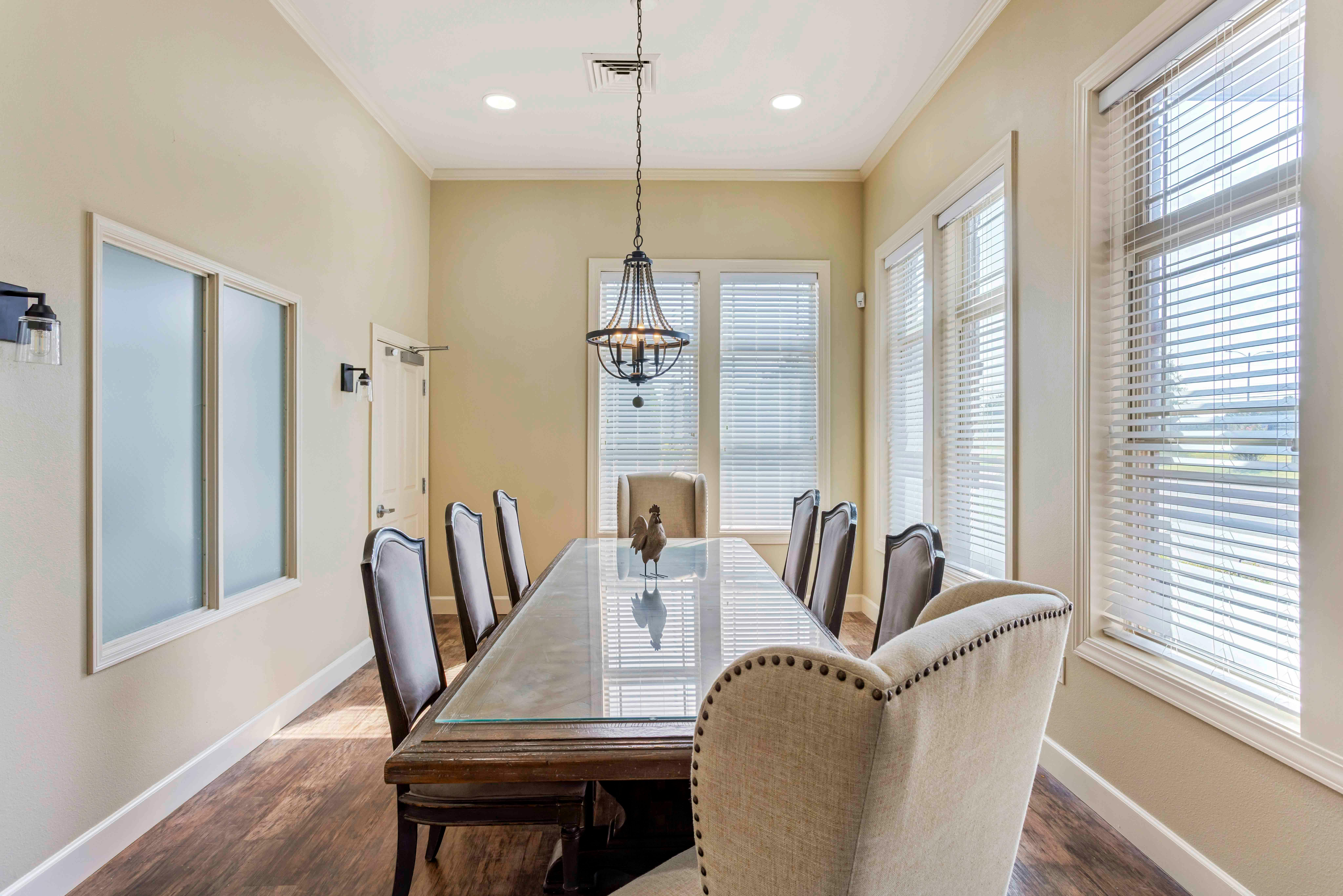 A long dining table with chairs, a light fixture, and windows with blinds