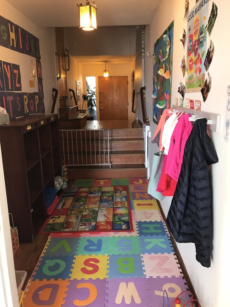Hallway with alphabet floor mats, coats on hooks, and a baby gate