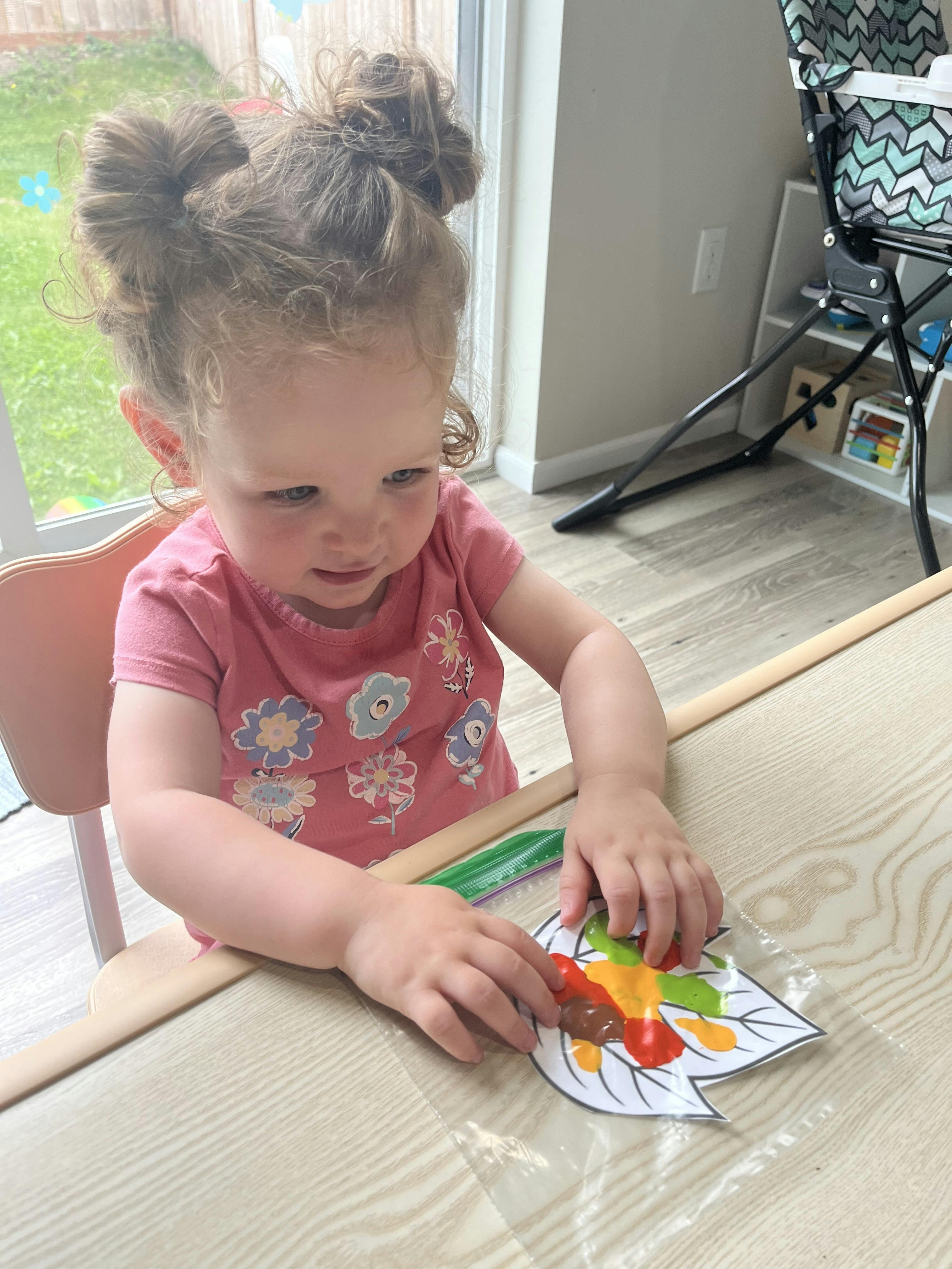 Child sitting at a table, pressing paint on a leaf-shaped craft