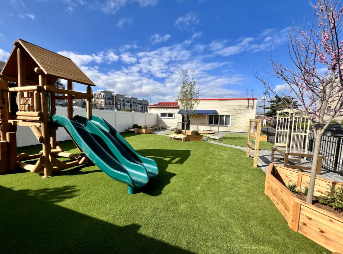 A playground with a wooden structure, two green slides, and artificial grass