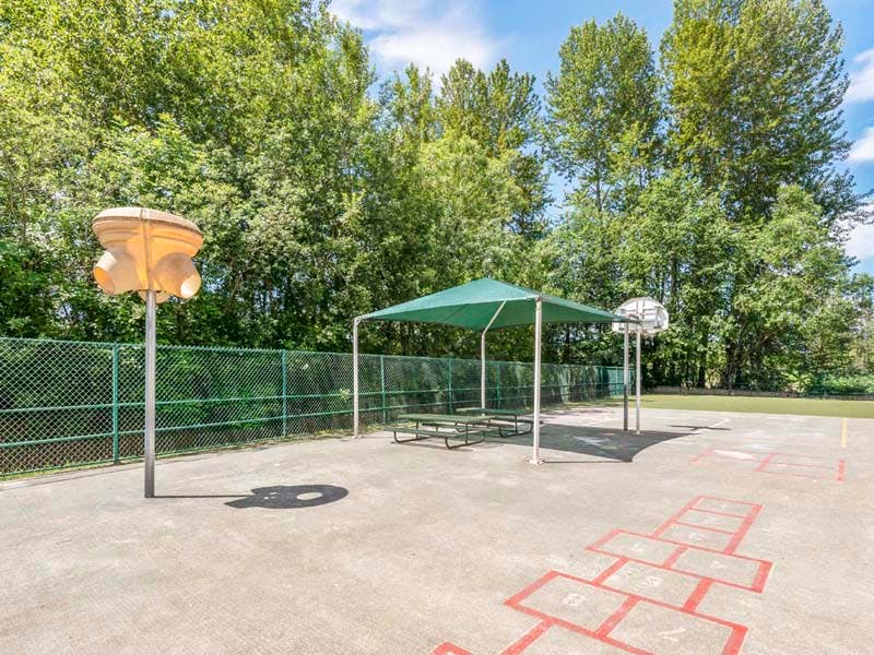 Playground area with a picnic table under a green canopy and a hopscotch court