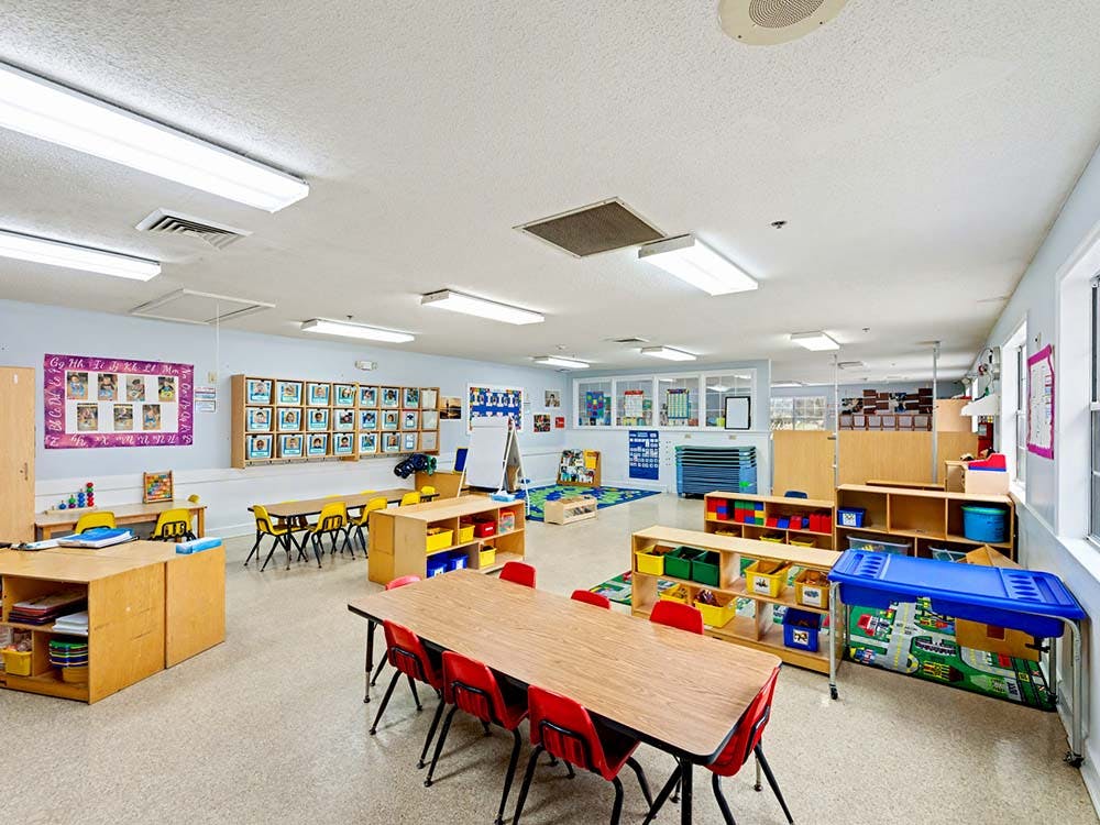 Empty classroom with small tables, chairs, and shelves filled with toys and supplies