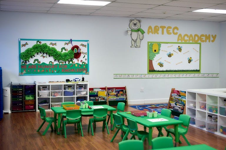 Classroom with green tables and chairs, bulletin boards, and storage shelves