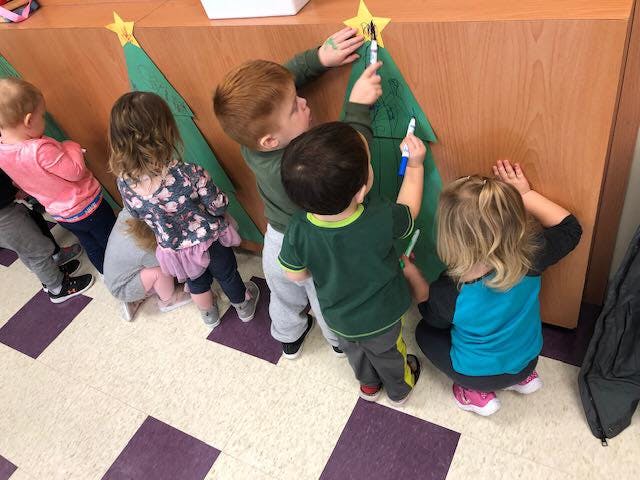Children decorating green felt trees with yellow stars