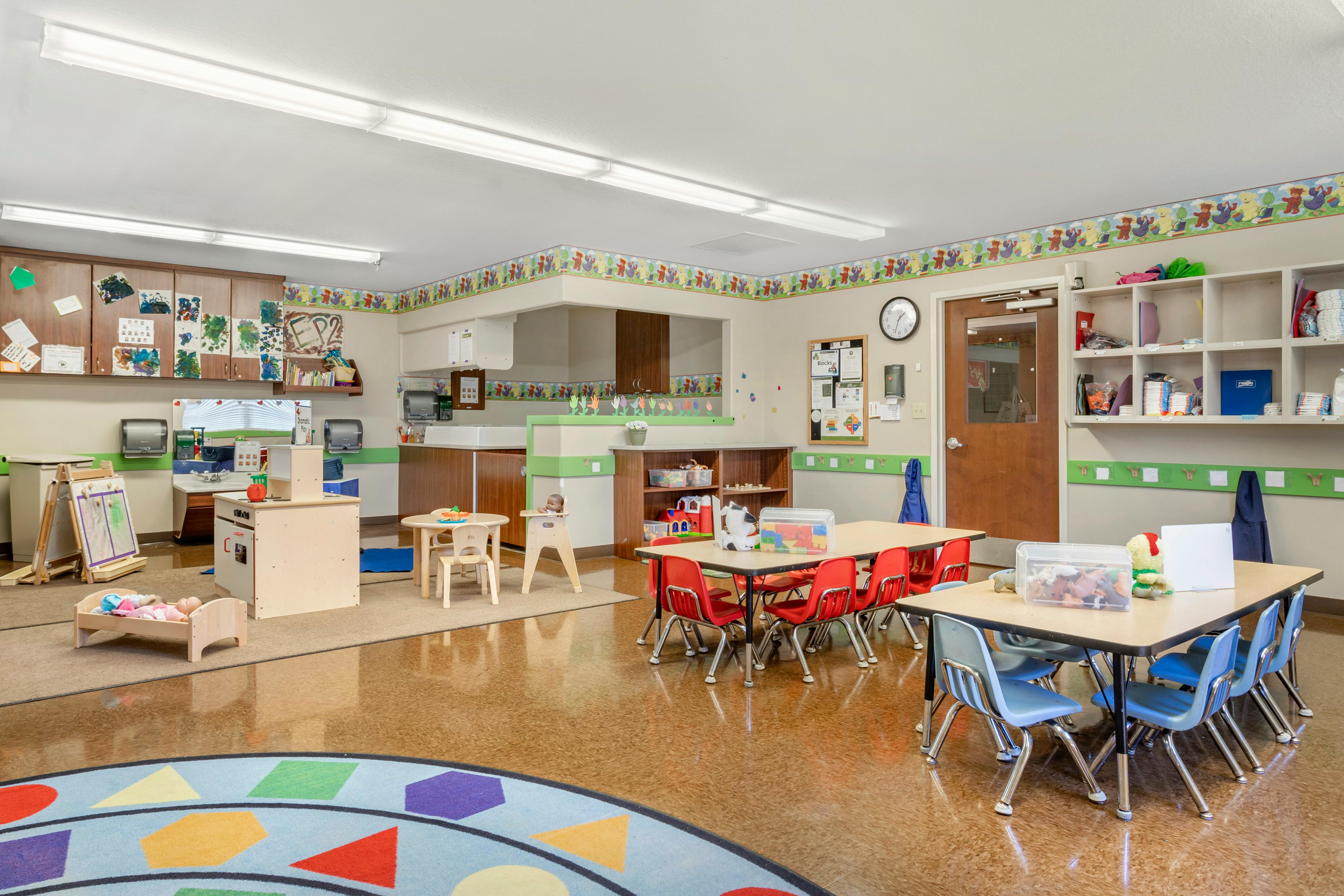 An empty childcare classroom with small tables and chairs
