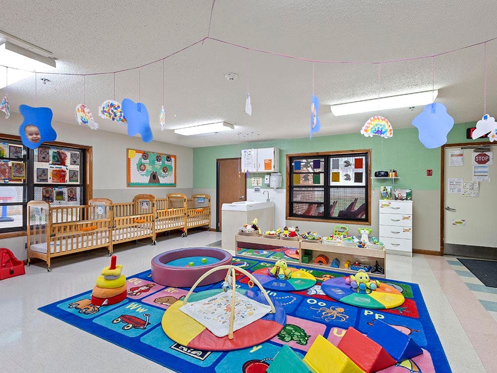 A colorful classroom with cribs, play mats, and hanging decorations