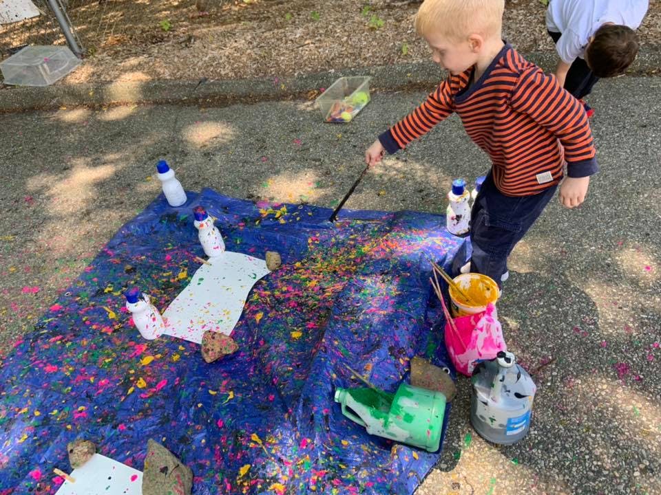 Child painting on a blue tarp with colorful paint splatters
