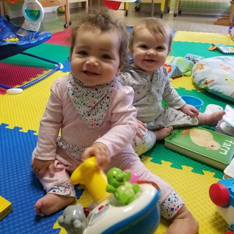 Two children sitting on a colorful mat playing with toys