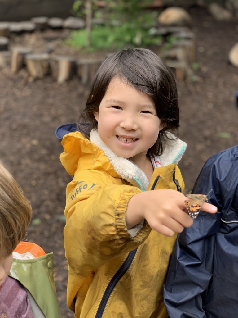 Child in yellow jacket with a butterfly on their finger