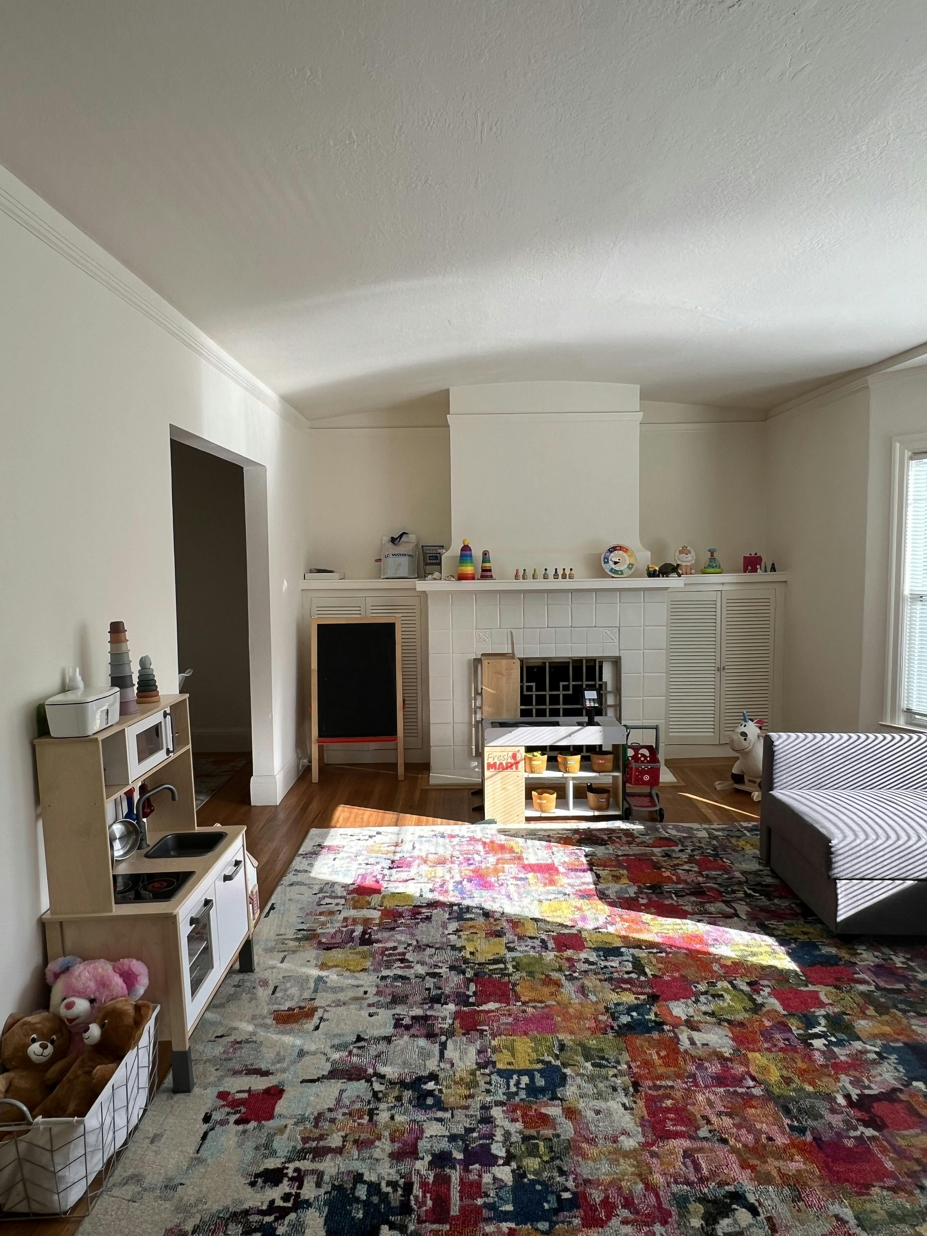 Living room with a colorful rug, fireplace, and child's play kitchen