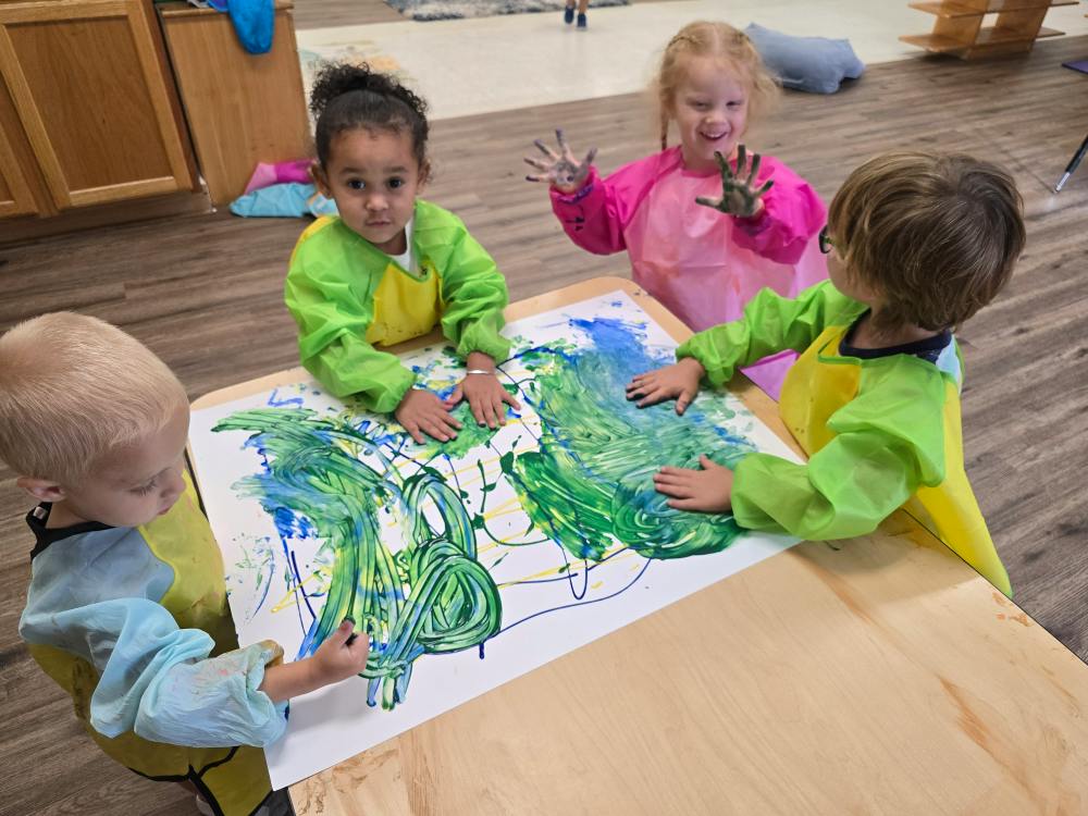Four children in art smocks finger painting on a table