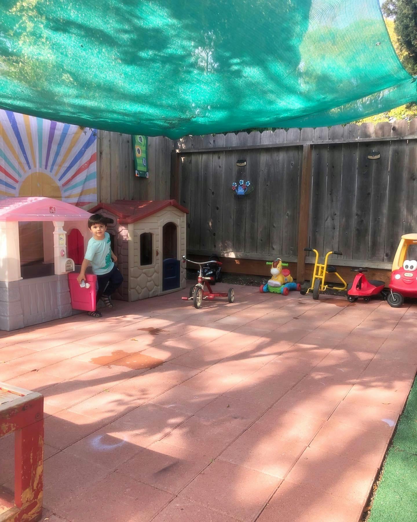 Child standing in an outdoor play area with playhouses and toys