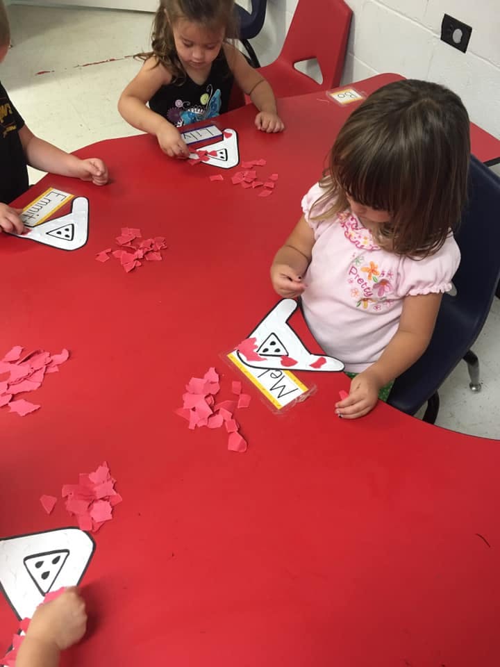 Children at a red table doing a craft with paper shapes
