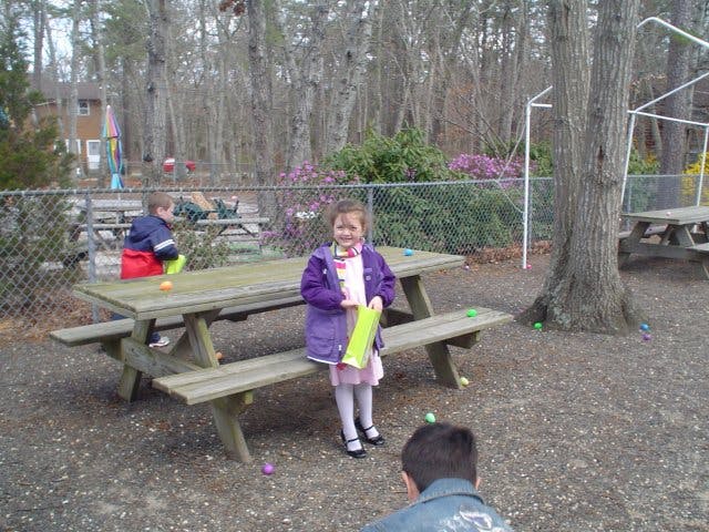 Child standing by a picnic table holding a yellow object