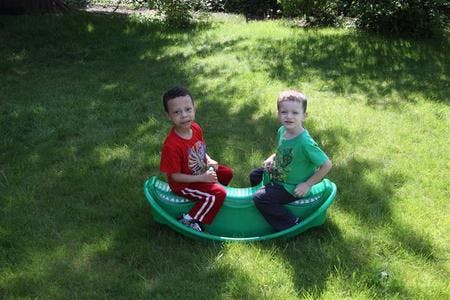 Two children sitting on a green seesaw in grass