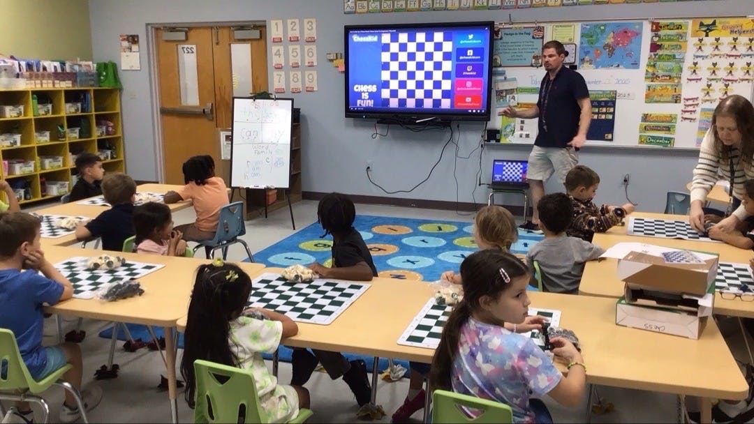 Children and adults in a classroom with chess boards