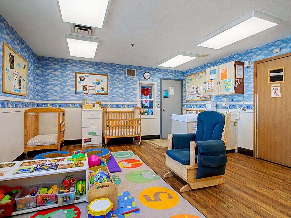 Classroom with two cribs, a rocking chair, and a rug with large numbers