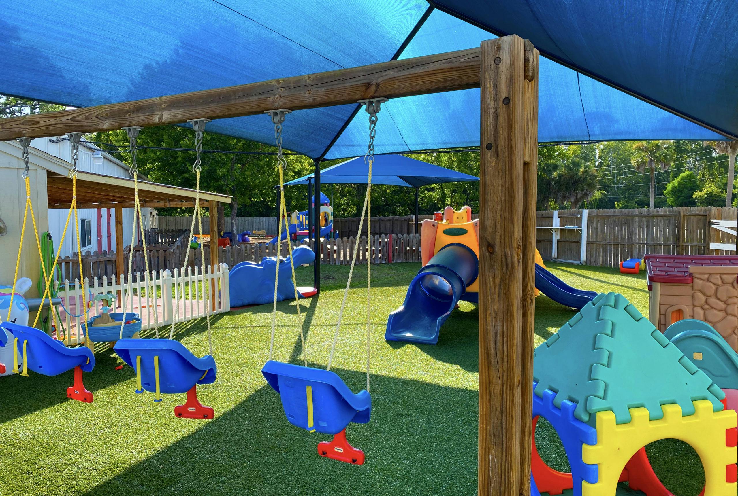 Swings and a slide on a playground with artificial turf under a blue shade covering