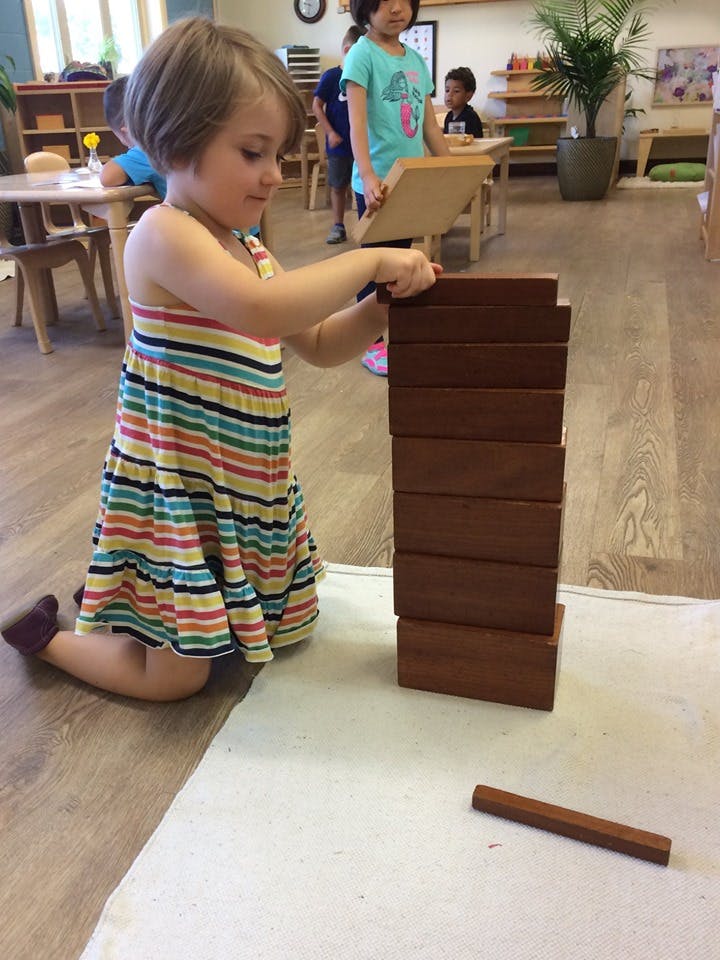 Child kneeling and stacking wooden blocks in a classroom