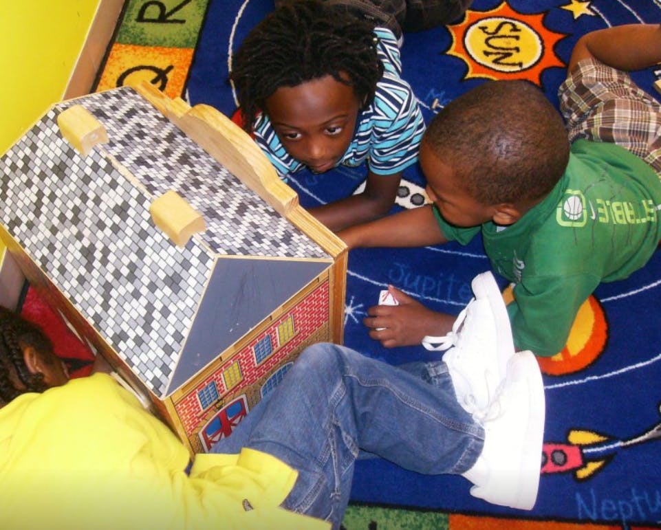 Three children playing with a dollhouse on a rug