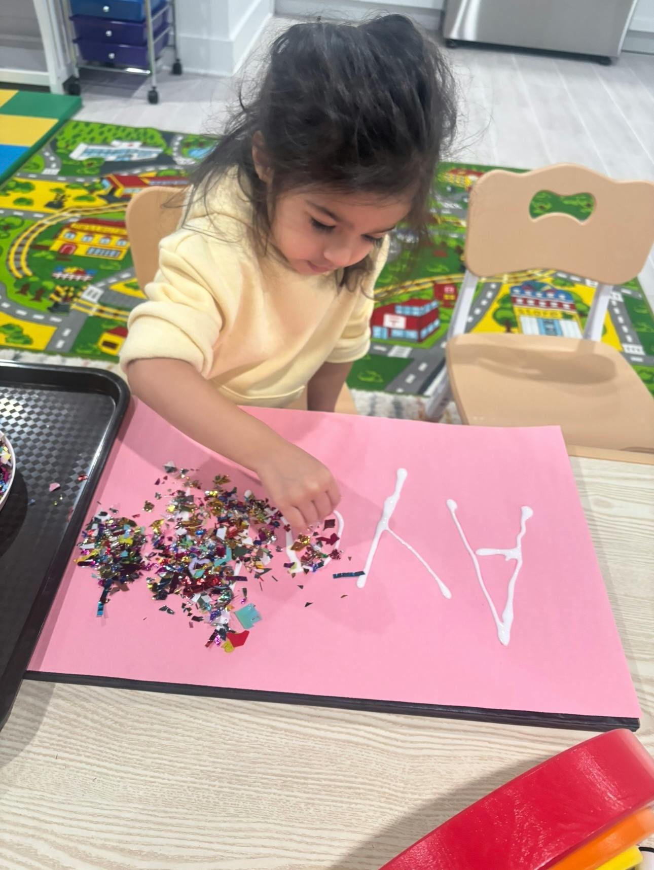 Child crafting with confetti and glue on pink paper