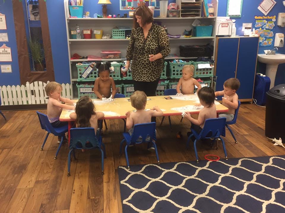 Adult standing over children seated at a table in a classroom
