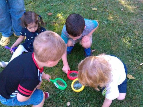 Four children looking at the ground with magnifying glasses