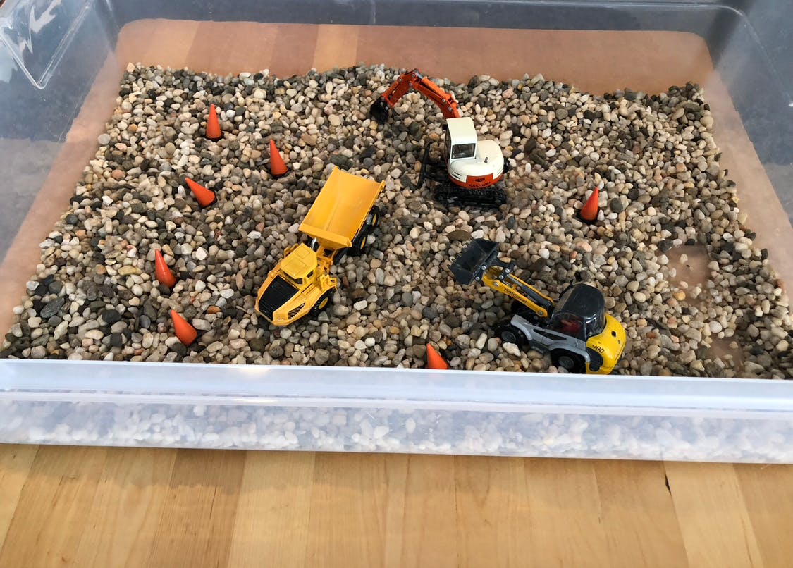 Construction toys in a bin of gravel with orange cones