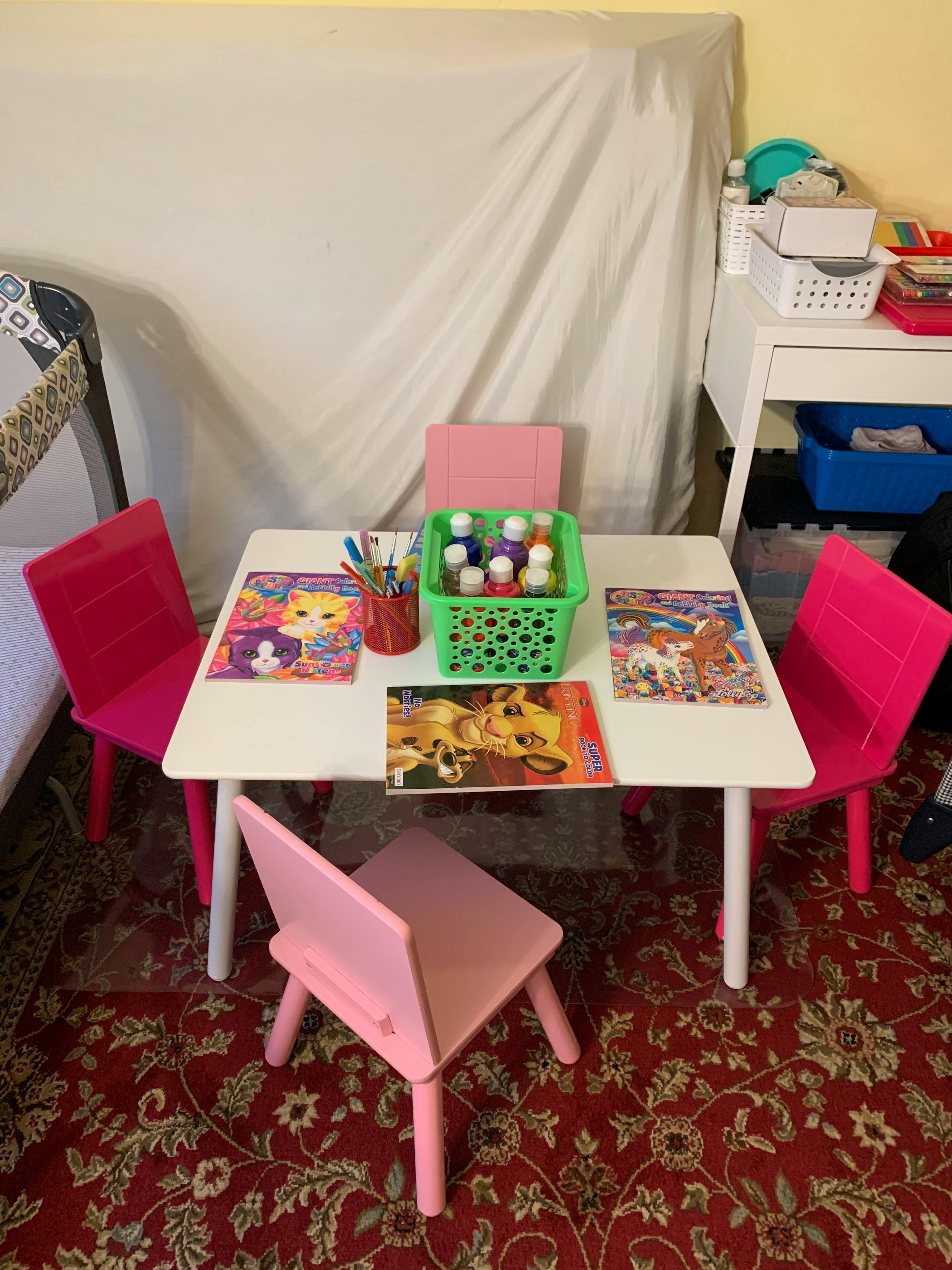 Small white table with four pink chairs, art supplies, and coloring books
