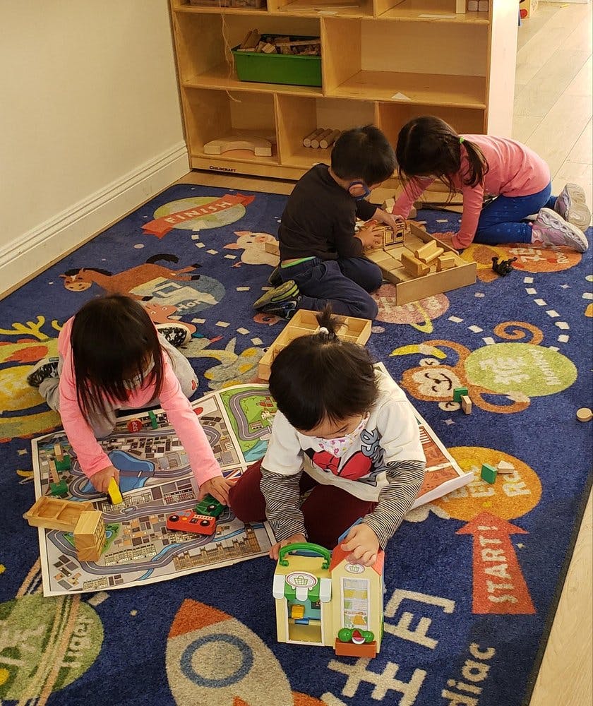 Four children playing with toys on a colorful rug in a classroom
