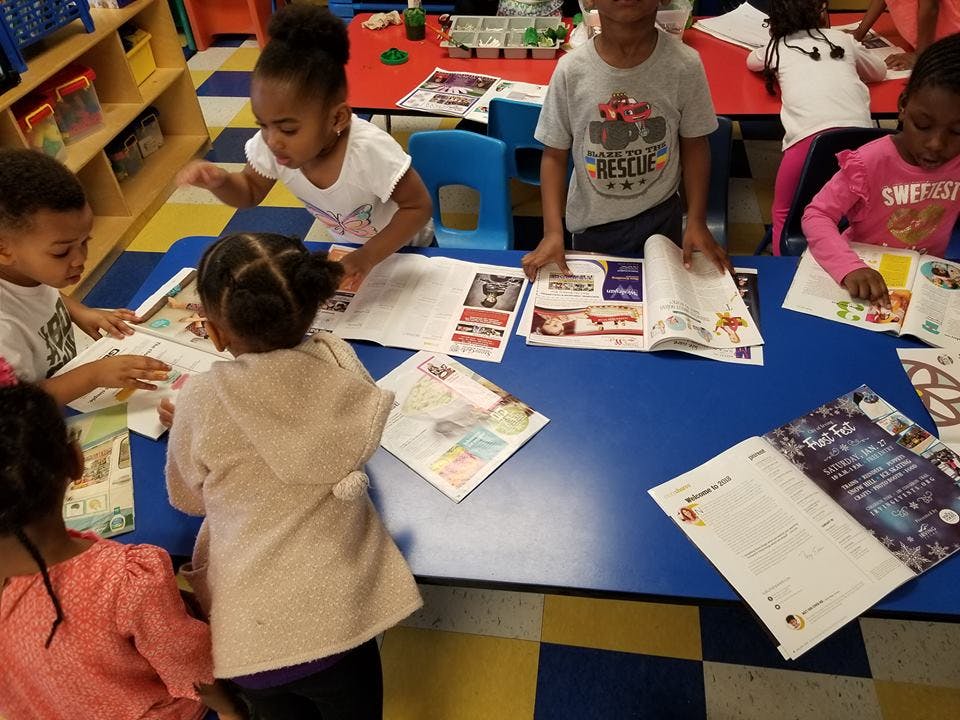 Children looking at papers and books on a blue table in a classroom