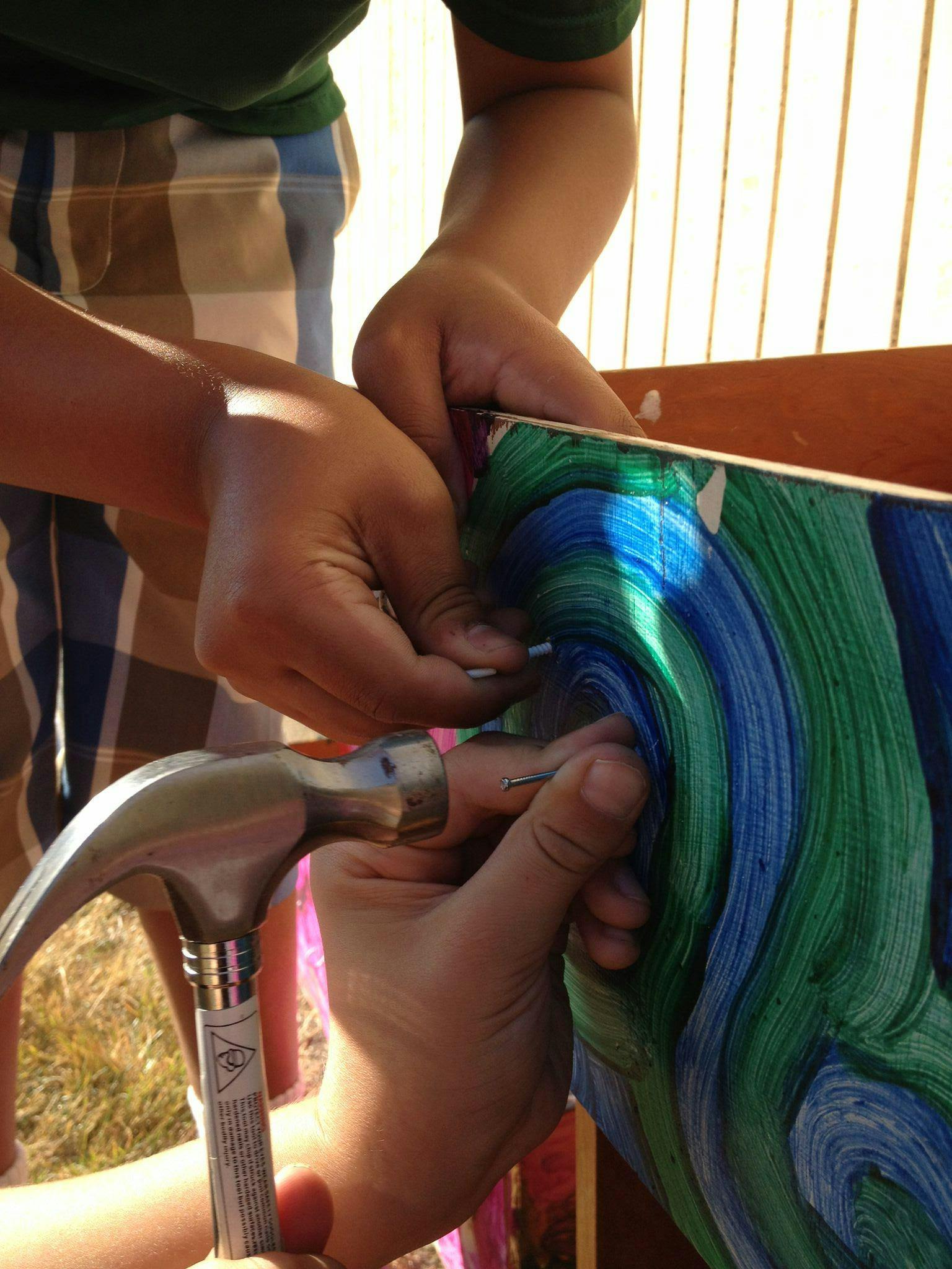 Person holding a nail and hammer to a colorful board