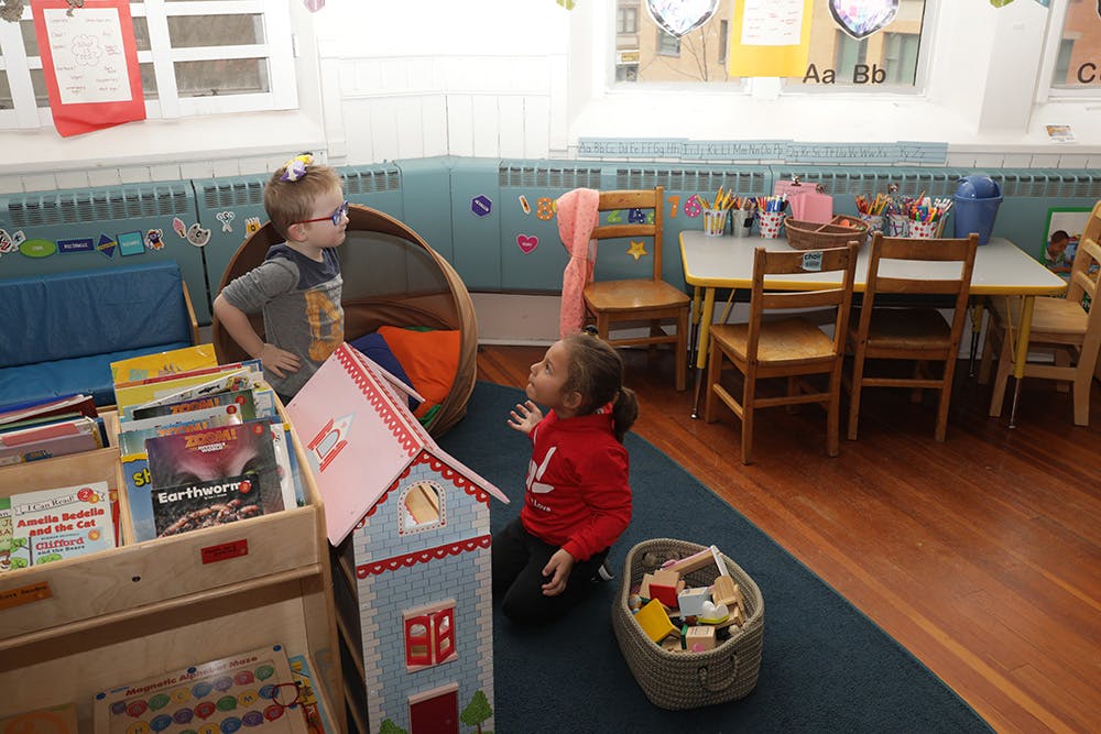Two children playing with a toy house in a classroom