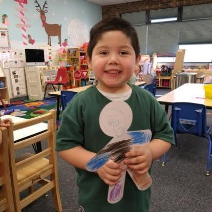 Child holding a paper cutout of a person in a classroom