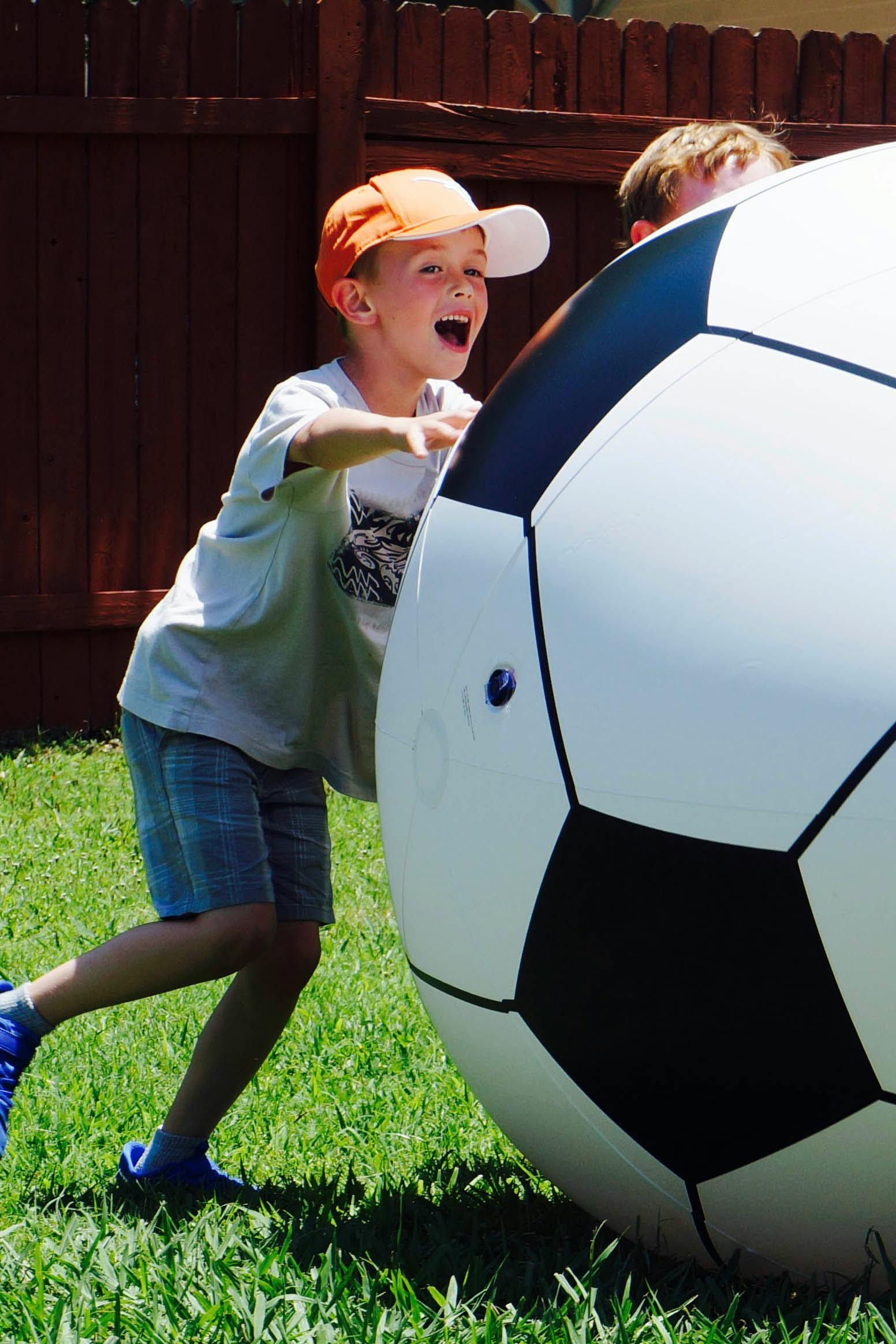 Child in a hat pushing a large soccer ball on grass
