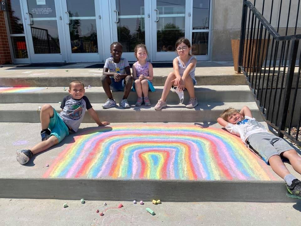 Children sitting and lying around a rainbow chalk drawing on steps