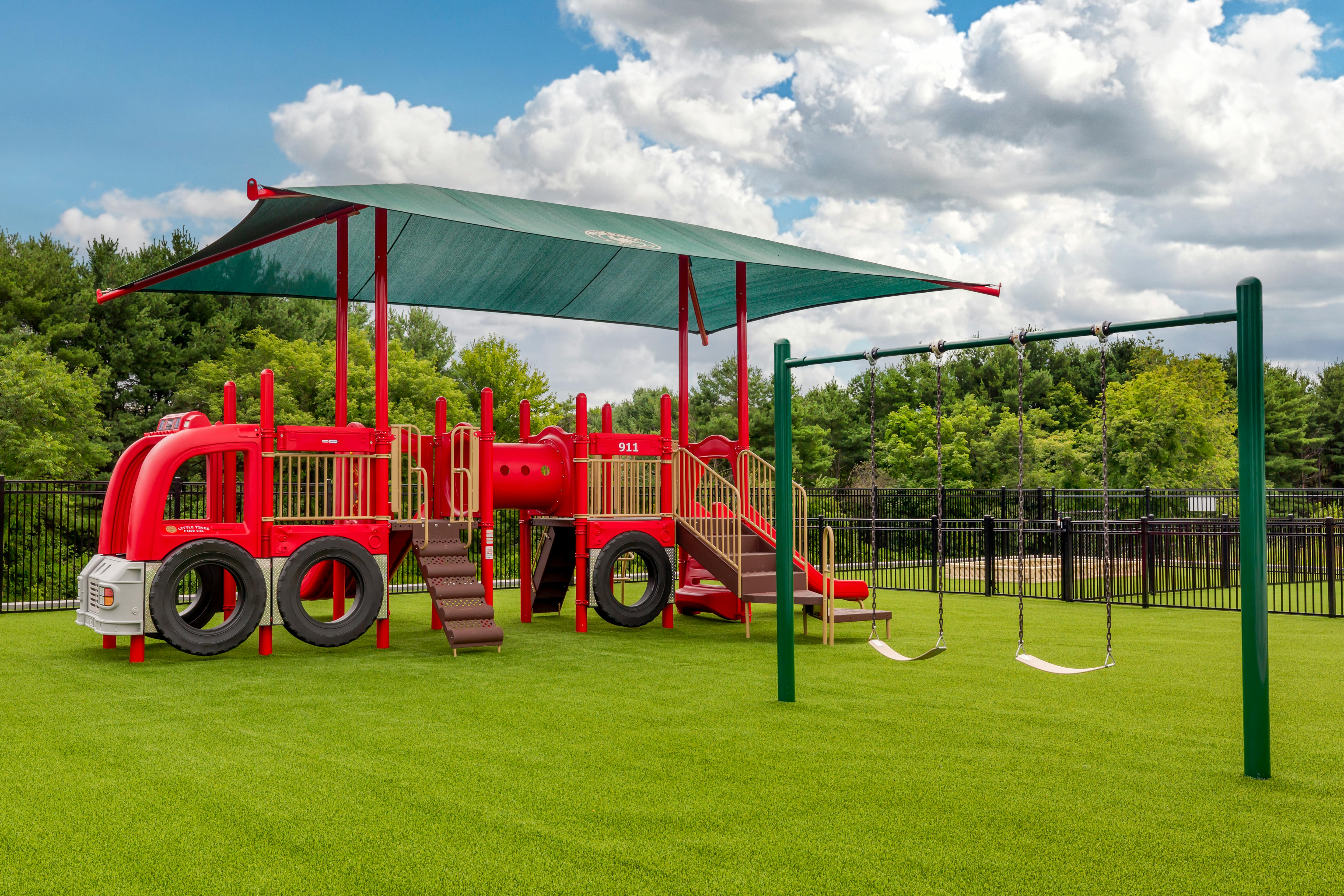 Red fire truck-themed playground with swings on artificial grass
