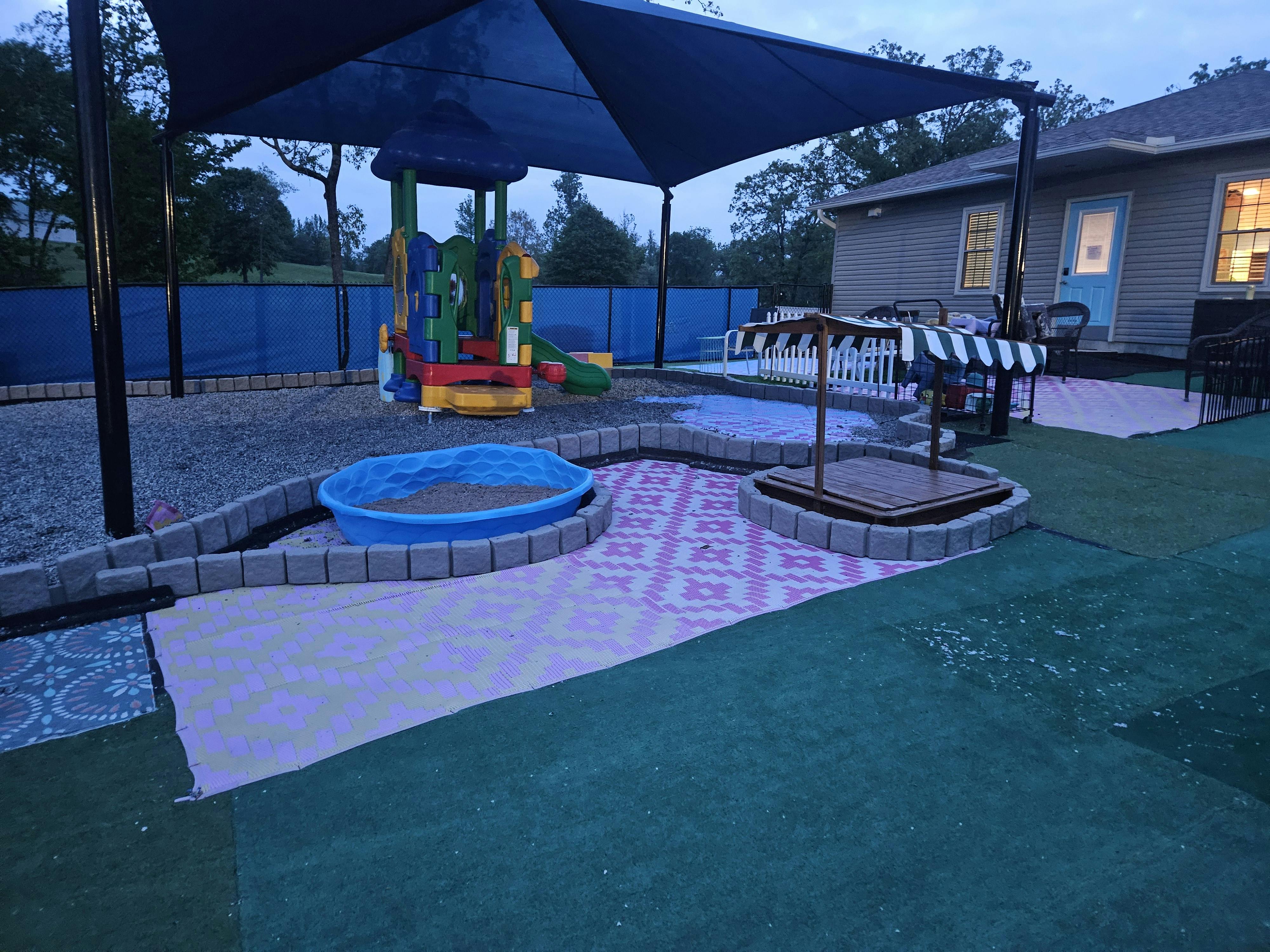 Outdoor play area with a colorful playset, sandboxes, and a shaded canopy